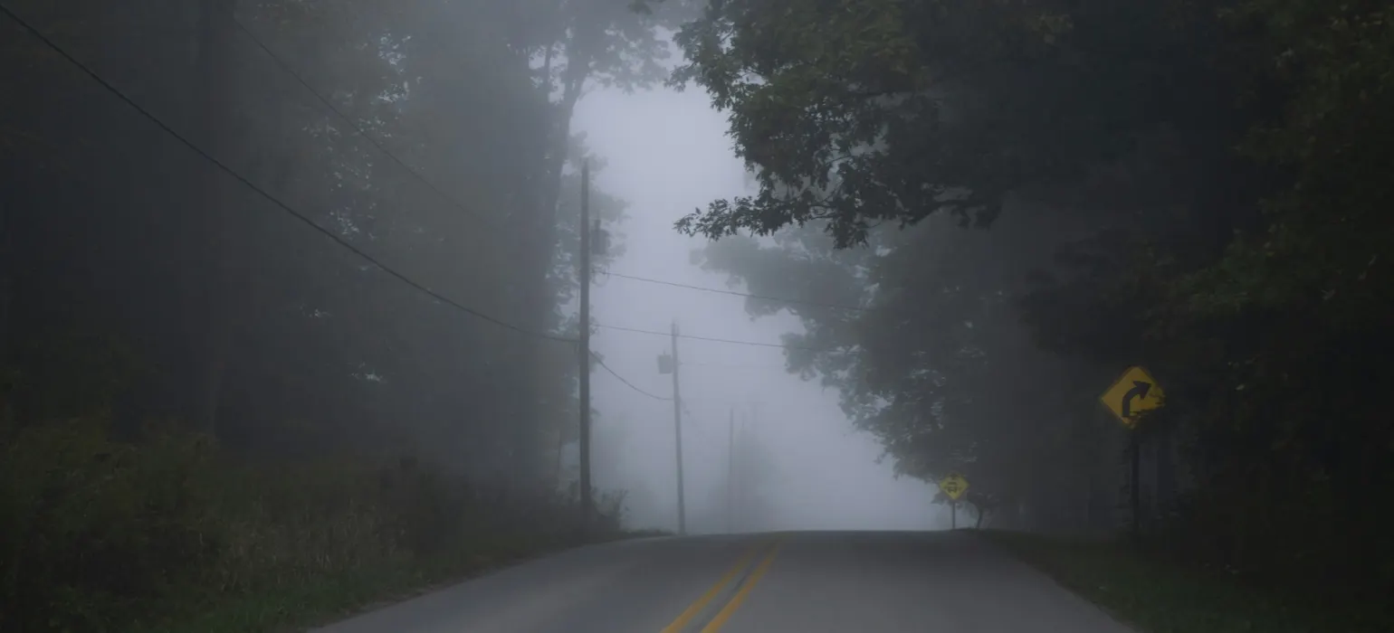 A foggy road with a yellow sign on the side