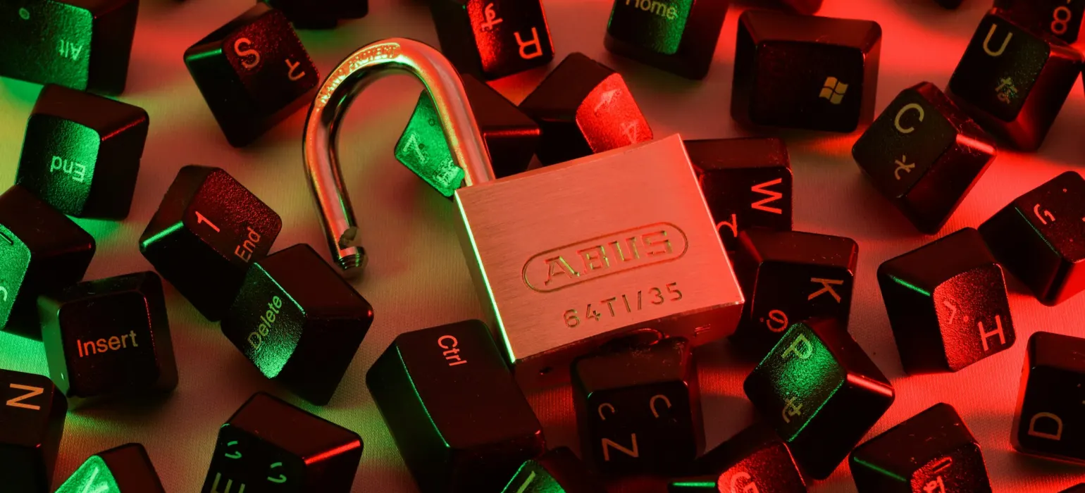 An open padlock surrounded by scattered black computer keyboard keys under red and green light