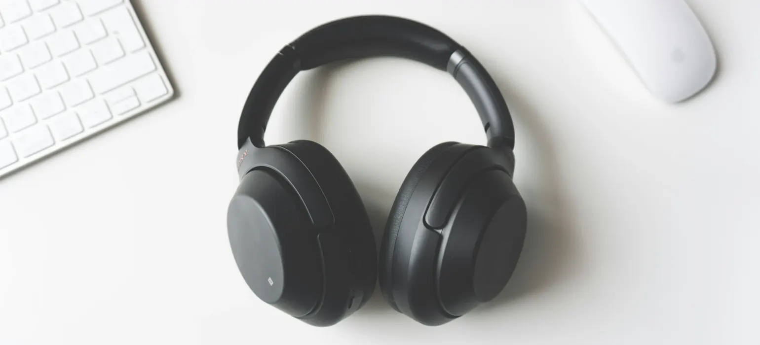 Black wireless headphones between a keyboard and mouse on a white surface