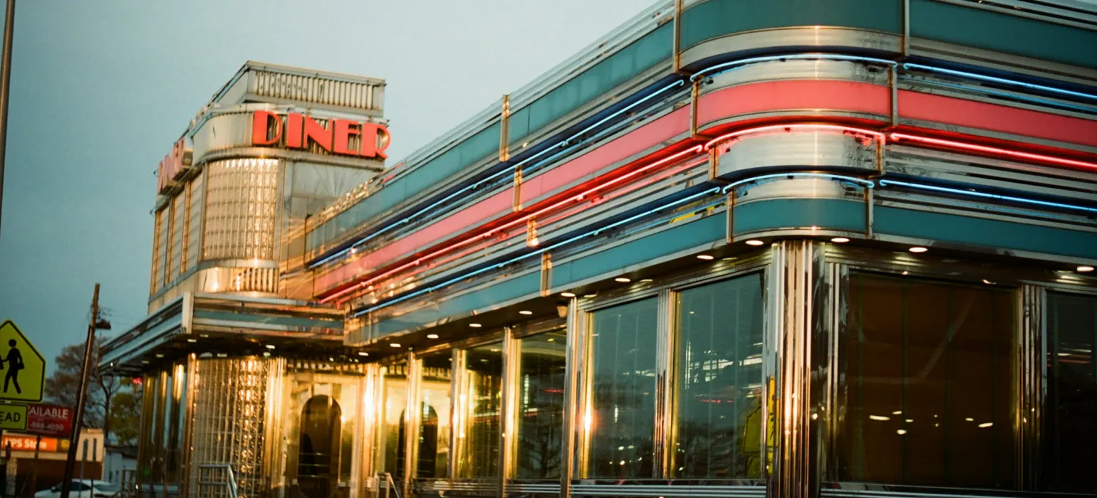 A retro diner with chrome trim and neon lights at dusk