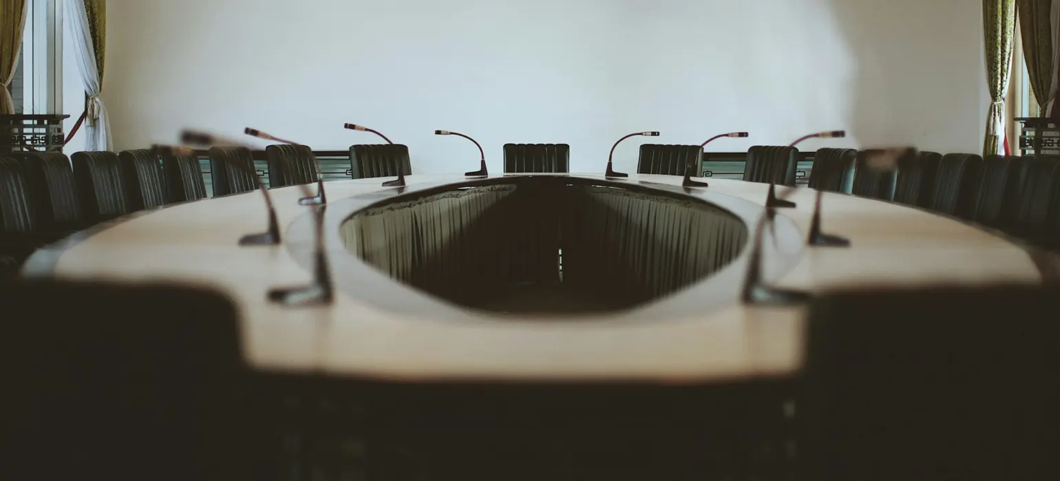 An empty conference table lined with microphones