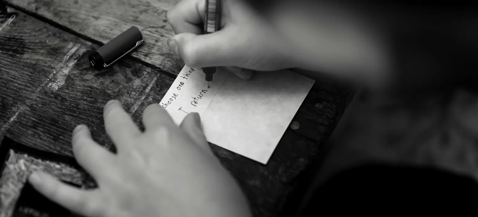 A person writing on a small card with a pen on a wooden table