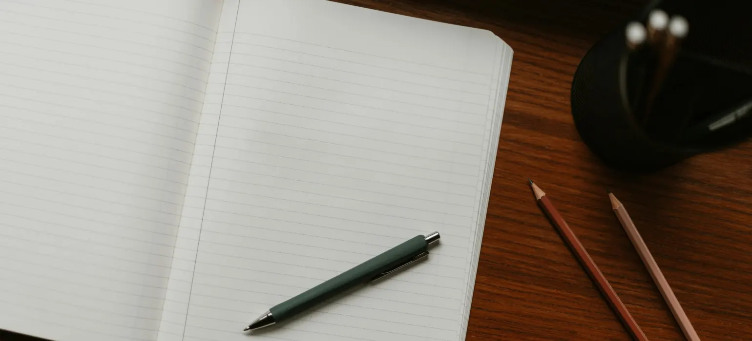 Open notebook with pen and pencils on desk