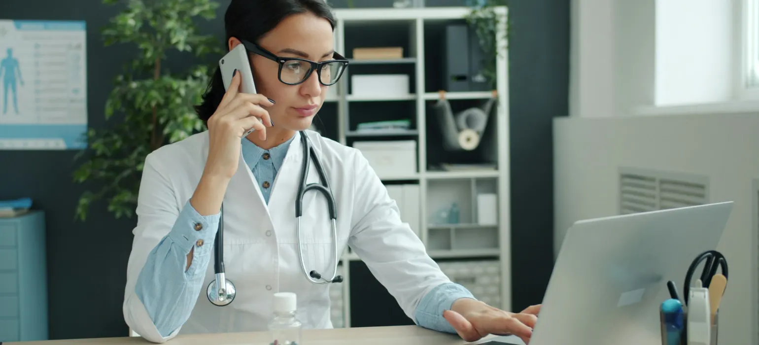 Doctor on phone, working on laptop in office