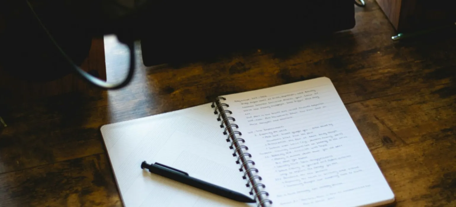 An open notebook with a pen on a wooden desk