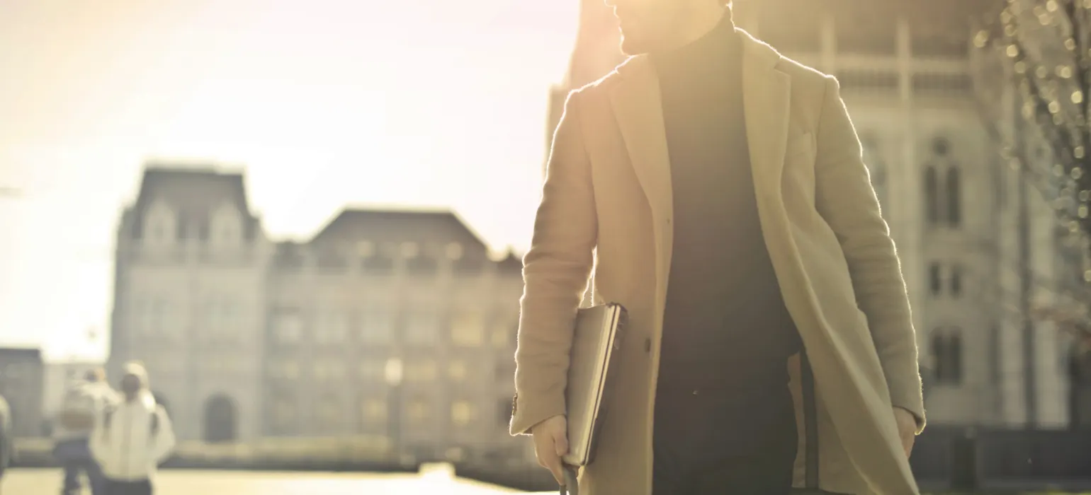 Professional in a coat walking through a city at sunrise