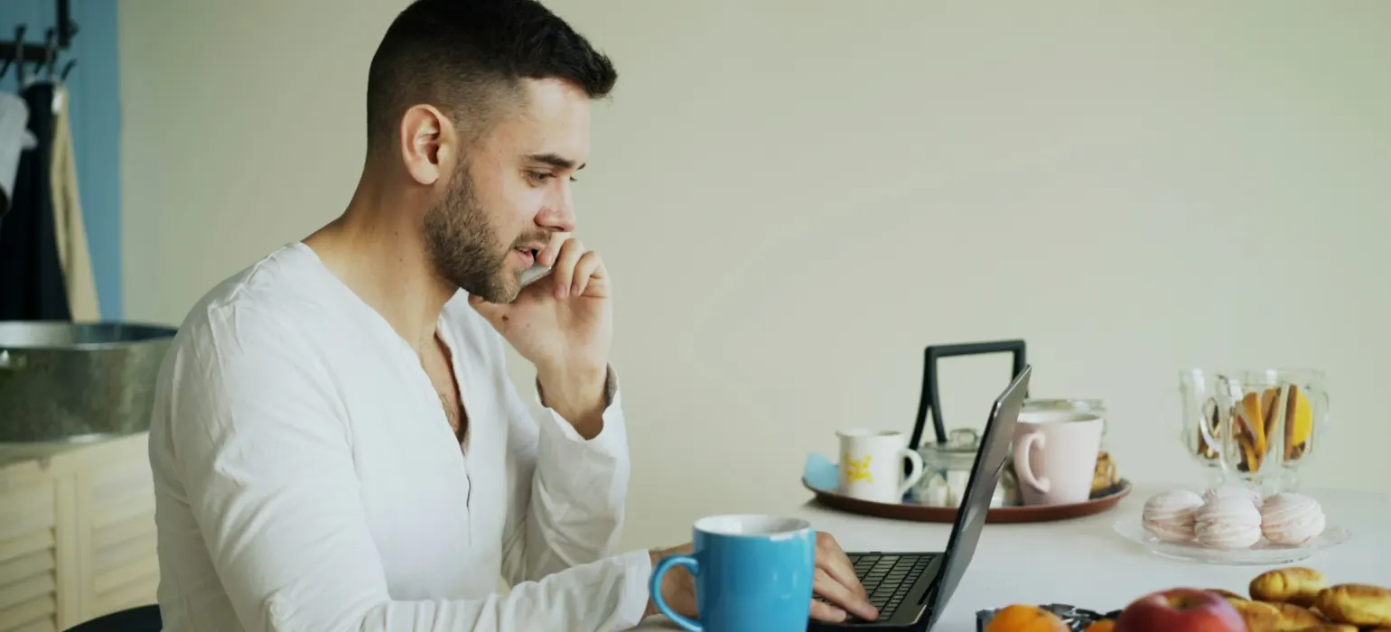 Man talking on phone while working on laptop at laptop
