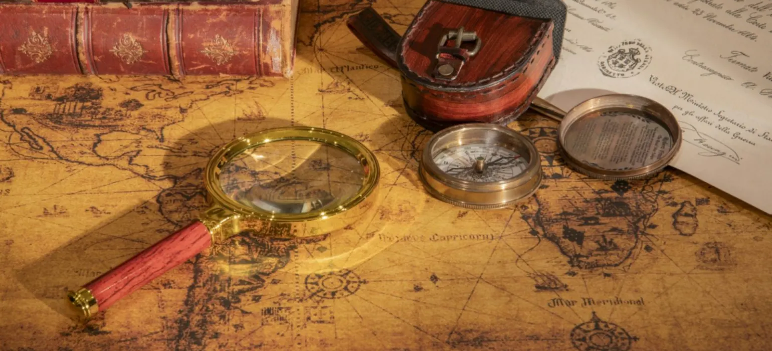 A magnifying glass and compass resting on an old map