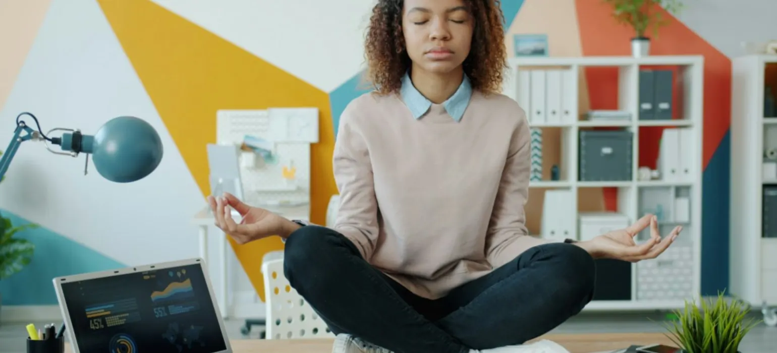 Woman meditating at a desk with laptop