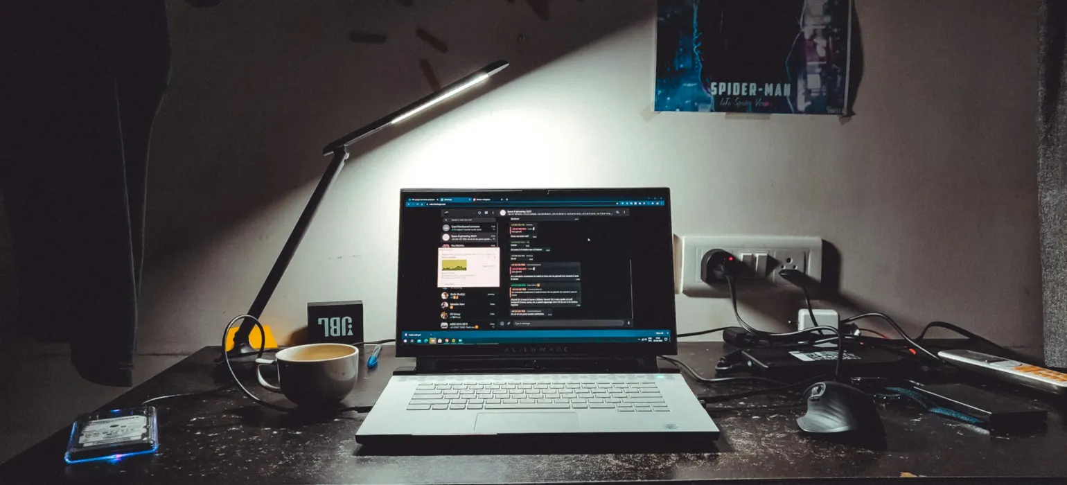 A laptop on a dark desk with a lamp, coffee cup, and mouse