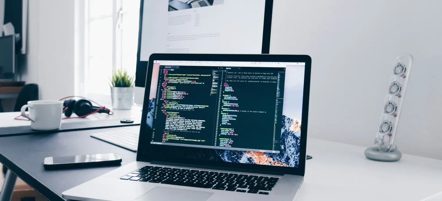 A MacBook with lines of code on its screen on a busy desk