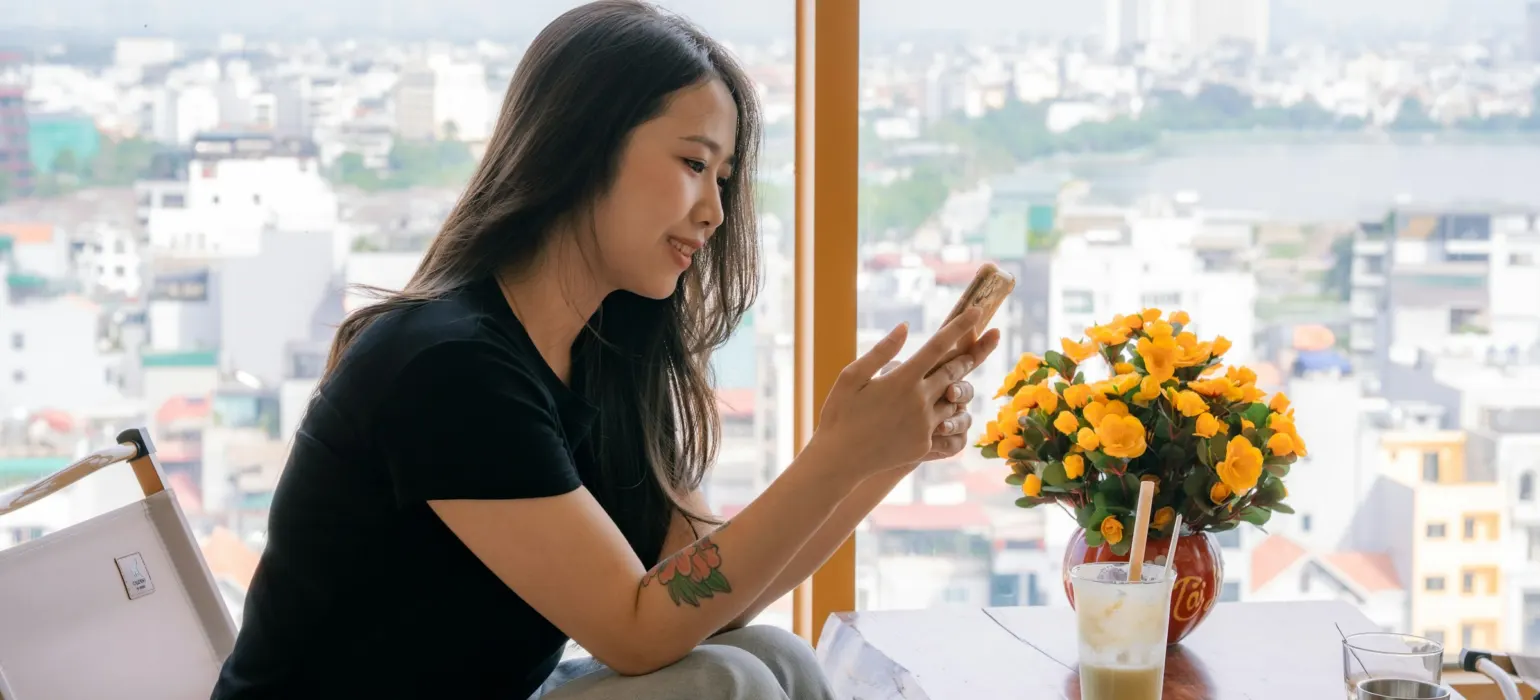 Young woman uses phone by window overlooking cityscape