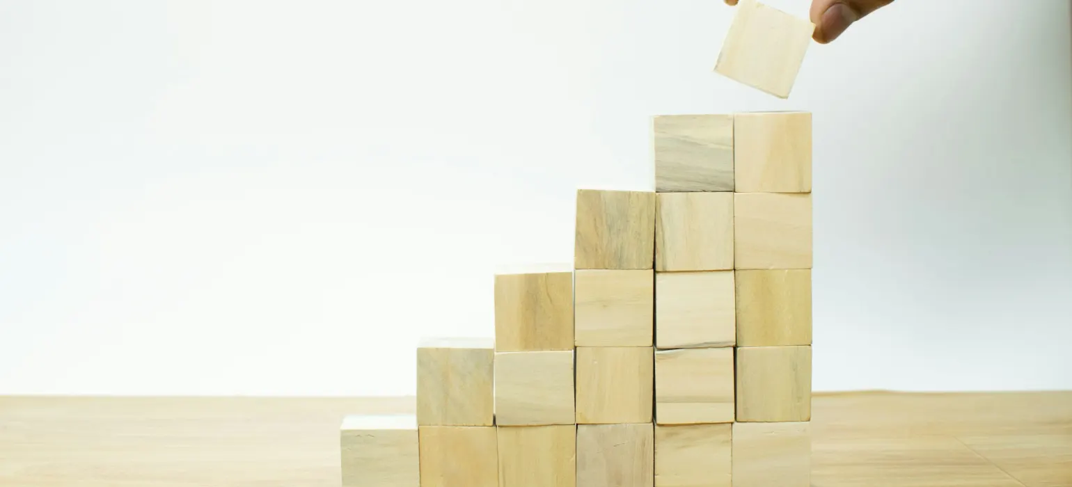 Hand placing a wooden block on a stepped pyramid of blocks