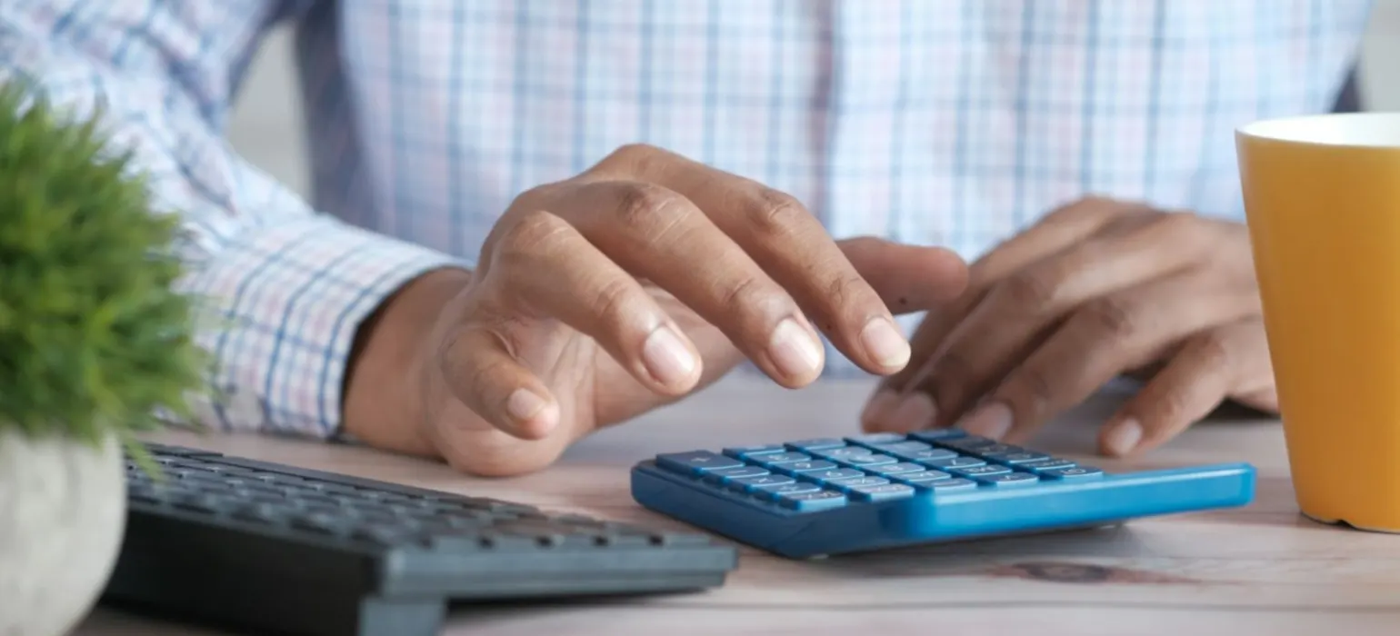Person using calculator at desk with coffee mug