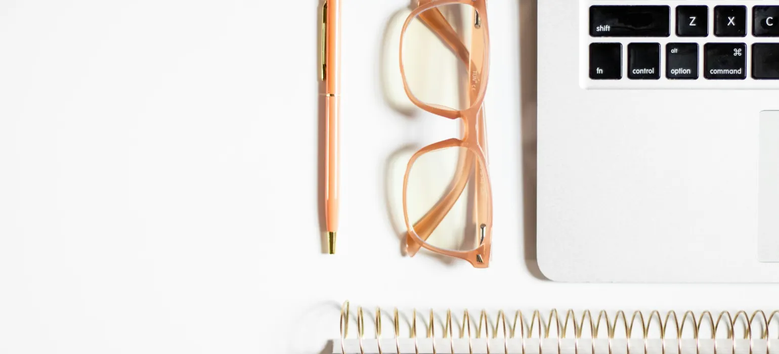 A desk with a laptop, glasses, and a notepad