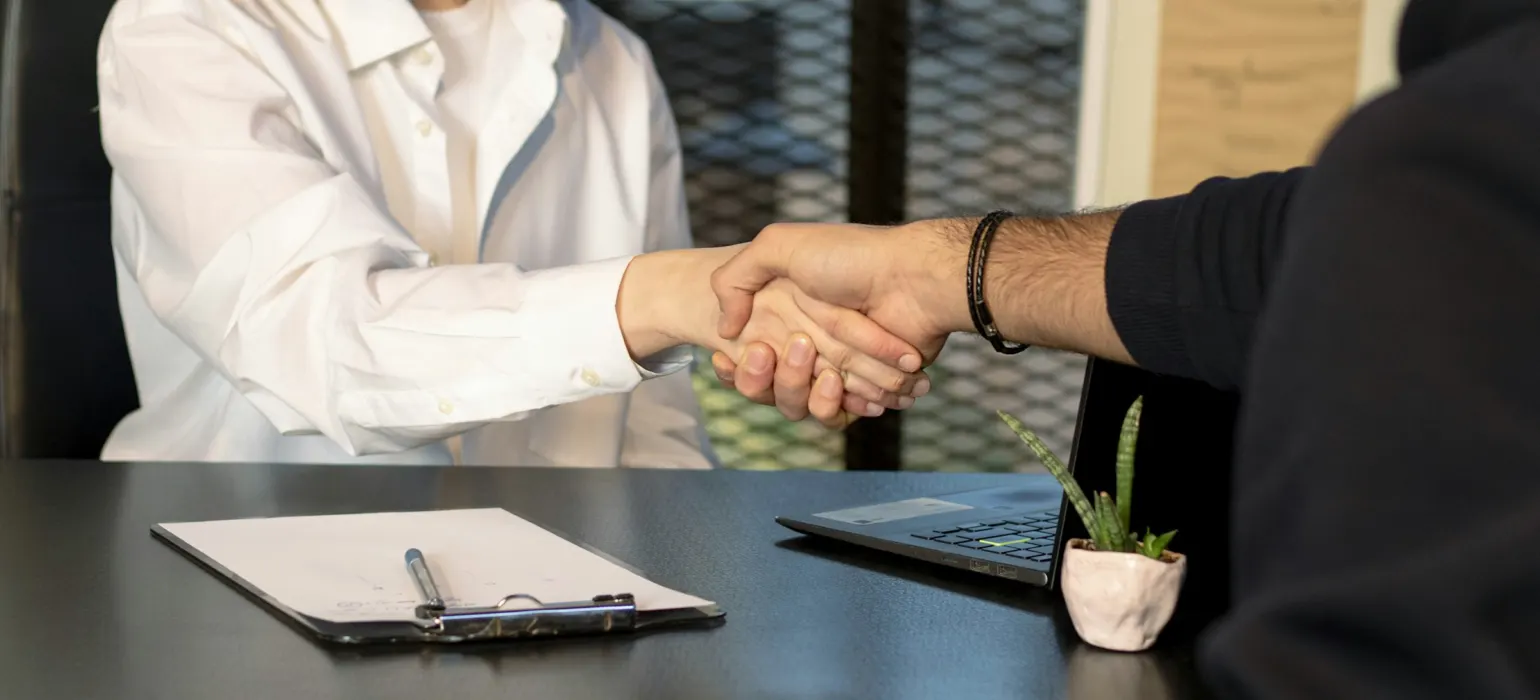 Two people shaking hands across a desk after a meeting