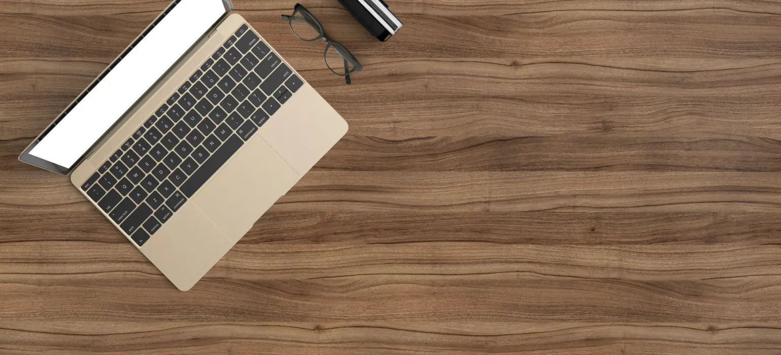 A laptop with a blank screen, glasses, and a small case on a wooden desk