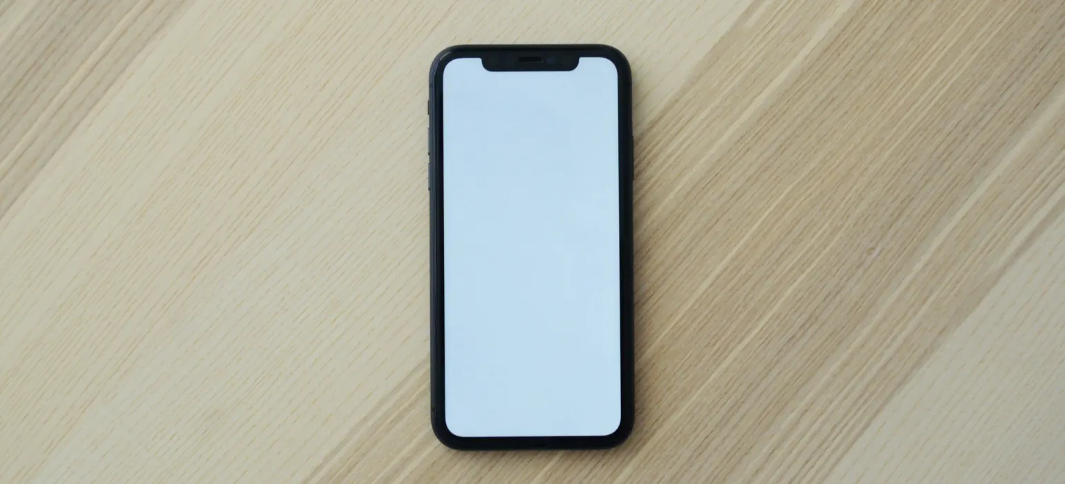 A black smartphone with a blank white screen on a light wooden surface