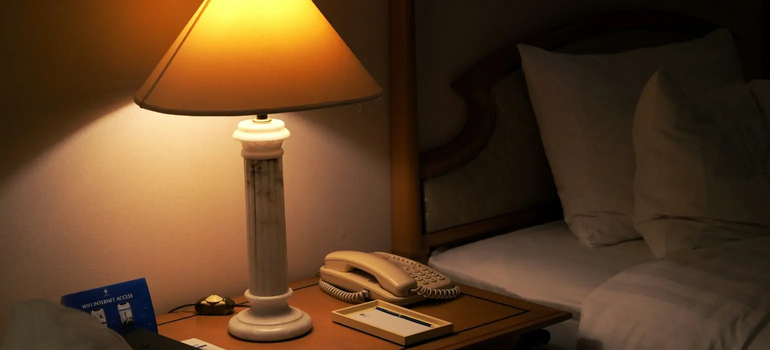 A lamp on a night stand next to a bed