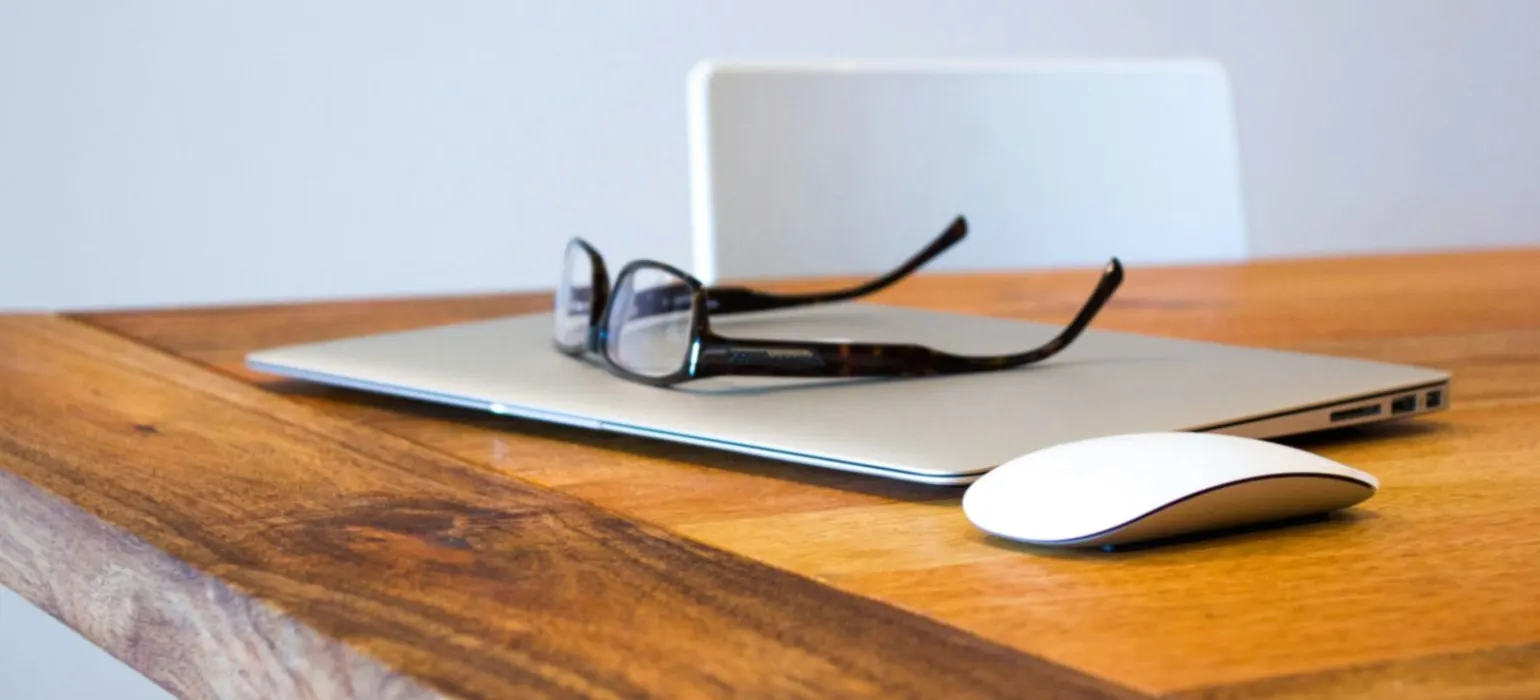 Glasses resting on a closed laptop on a wooden desk