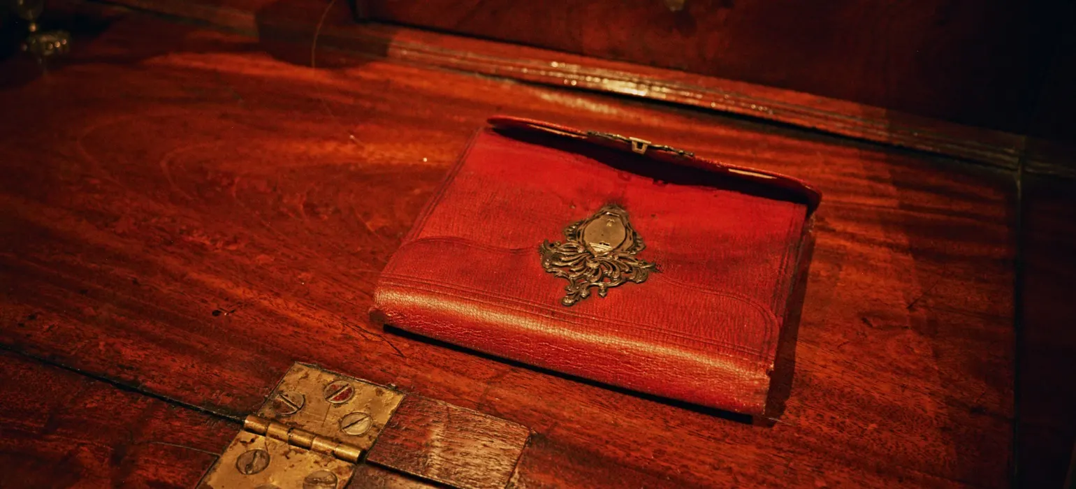 A red leather journal with an ornate metal clasp on a wooden desk