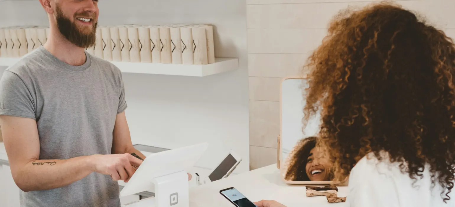 Shop owner smiling at a customer paying by phone at the counter