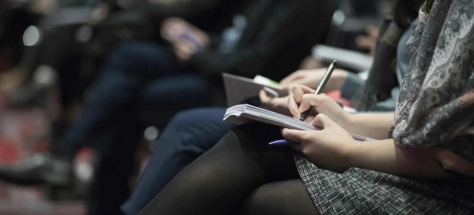 Person taking notes in a notebook at a press event