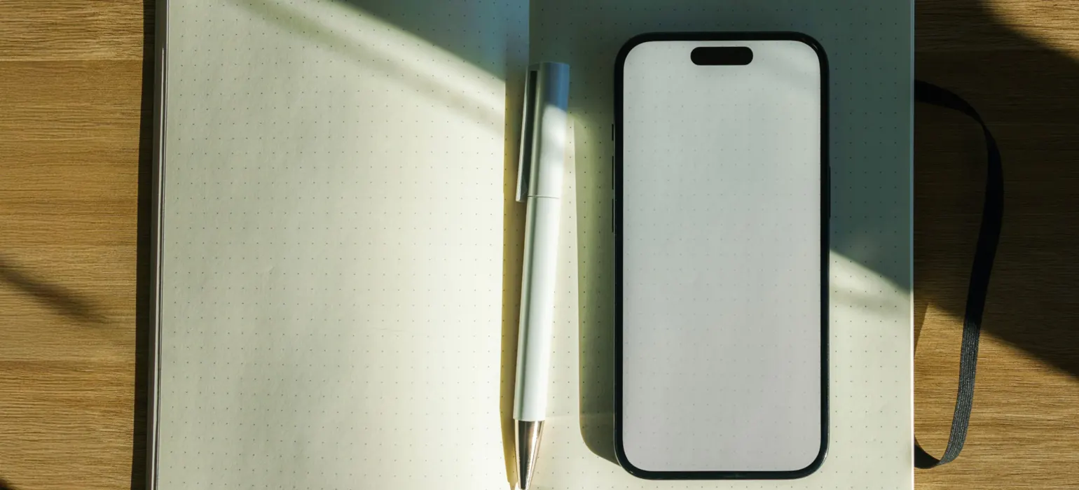 Notebook with pen and smartphone on wooden table