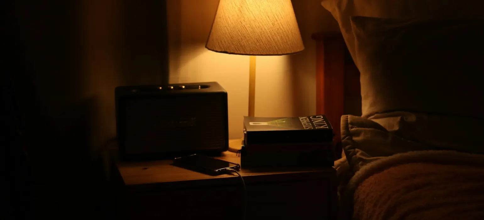 A bedside lamp illuminates a nightstand with a radio