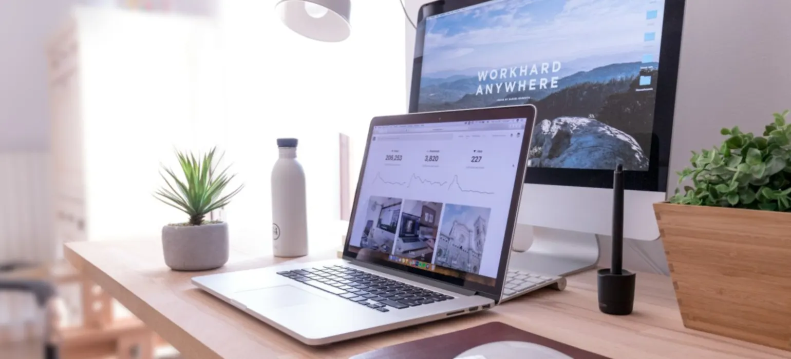 A laptop and desktop monitor on a bright wooden desk