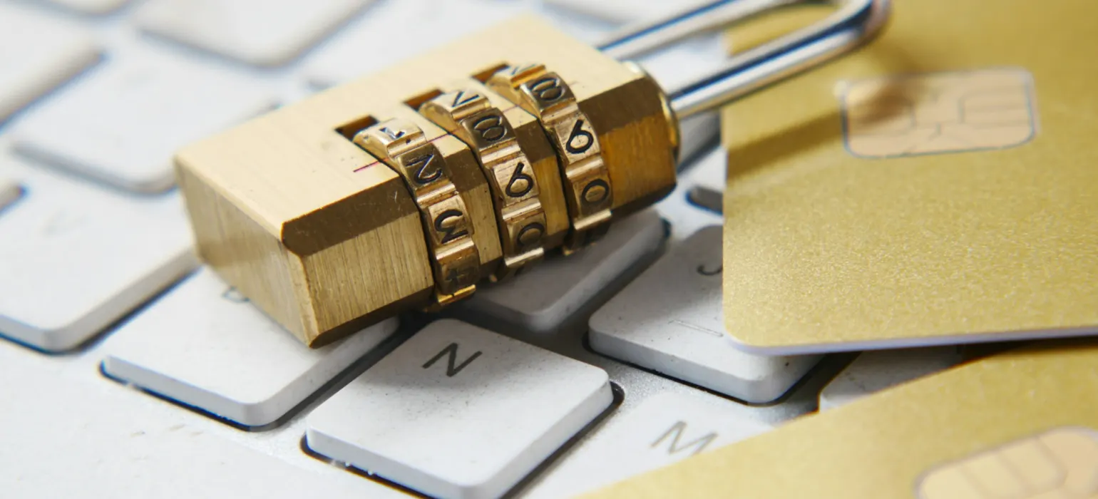 Gold padlock resting on a keyboard beside payment cards