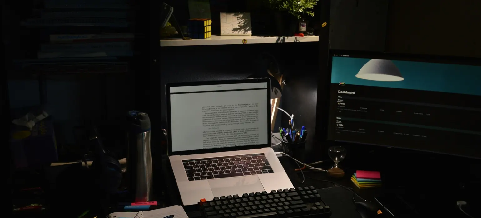 A laptop and monitor on a desk in a dim room