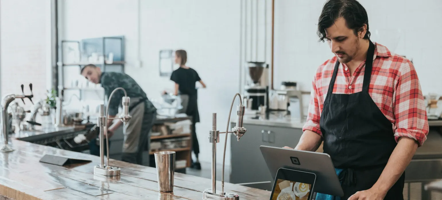 Cafe owner in an apron checking a tablet behind the counter
