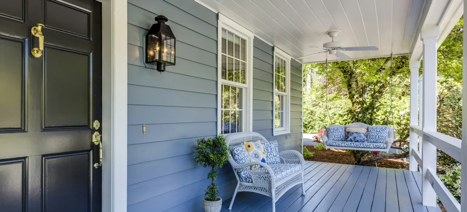A blue porch with a black door, white wicker furniture, and a hanging swing