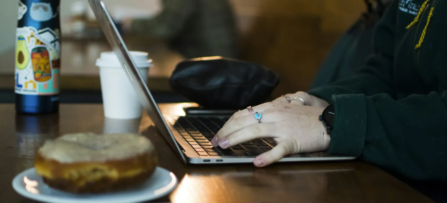 Person typing on a laptop at a cafe table next to a coffee cup