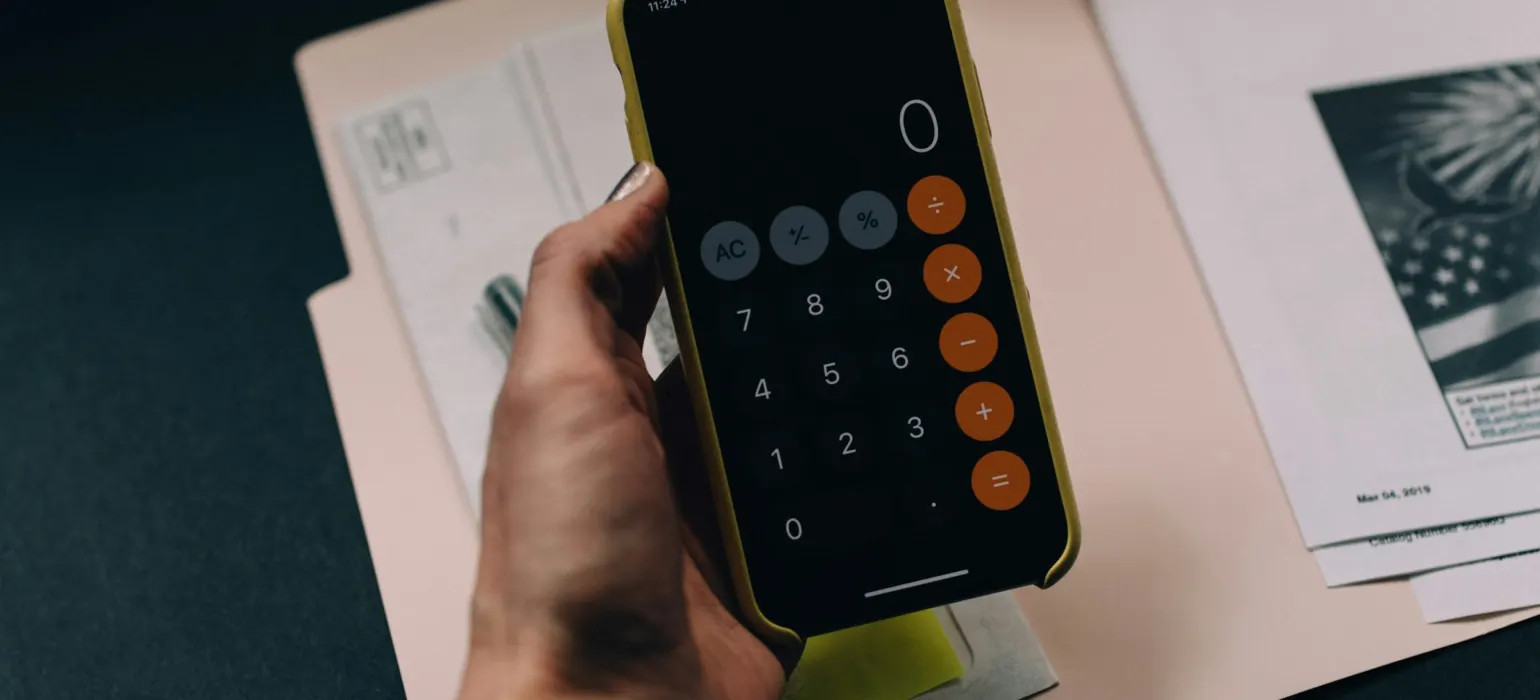 A hand holding a smartphone displaying a calculator app over a paper folder