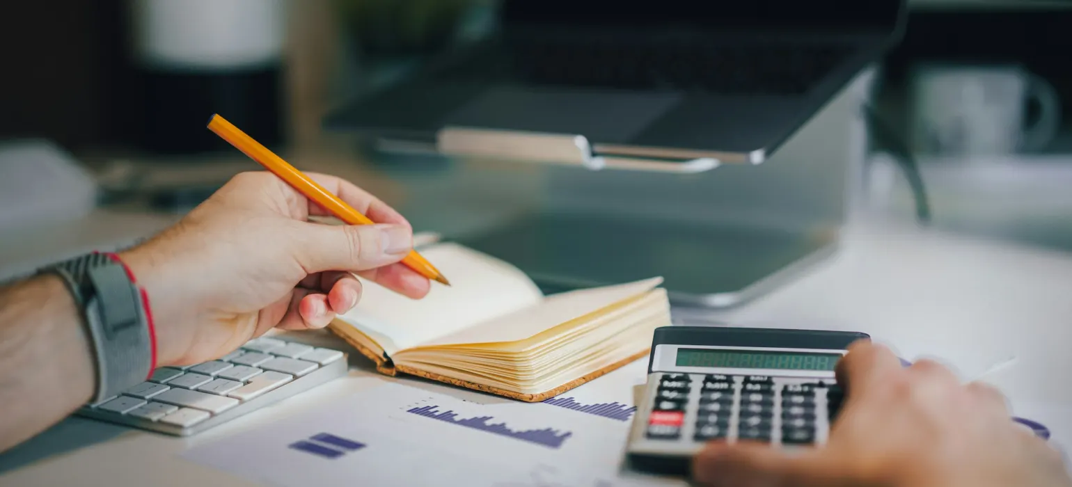 A person sitting at a desk with a calculator and a notebook