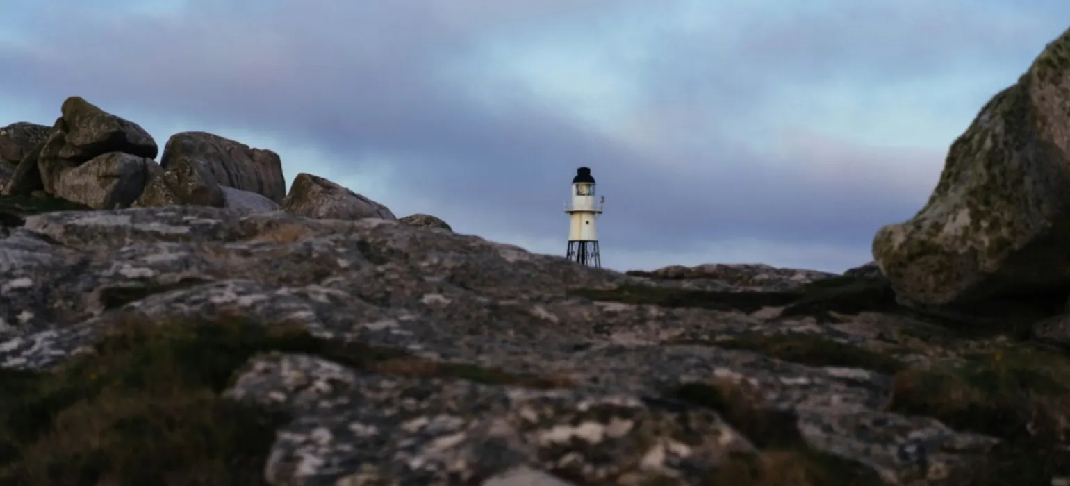 White lighthouse on a rocky coast under a cloudy sky