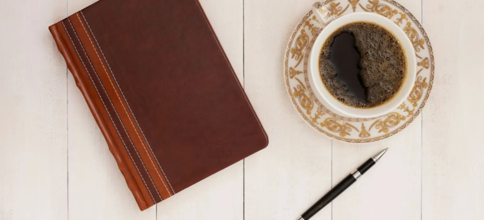 A cup of coffee next to a notebook and pen