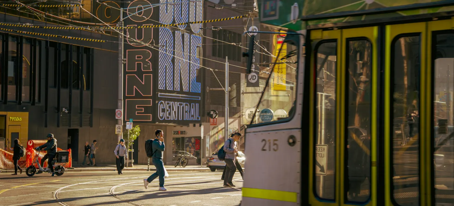 A yellow tram on a city street with pedestrians