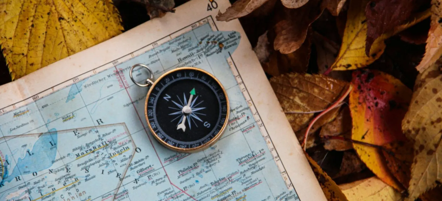 A compass resting on a map among autumn leaves