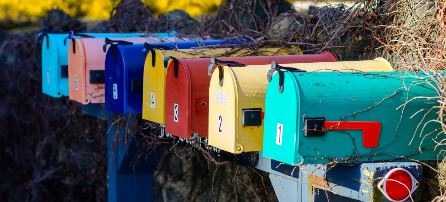 A row of colorful mail boxes sitting next to a bush