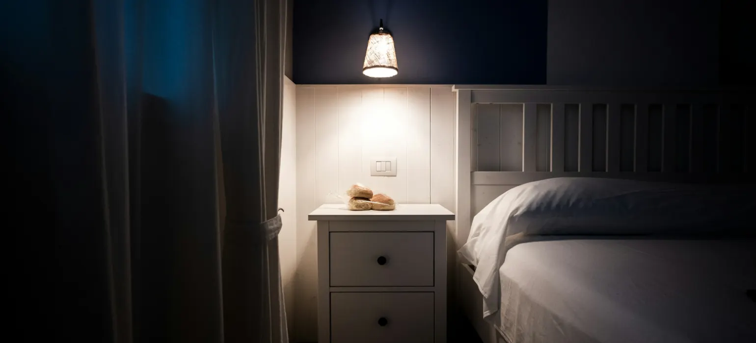 A bedside lamp illuminates a nightstand next to a bed
