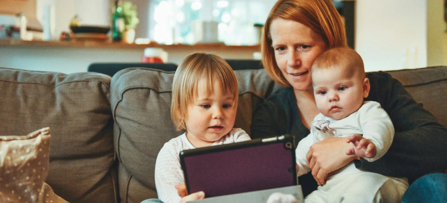 A parent and two young children looking at a tablet