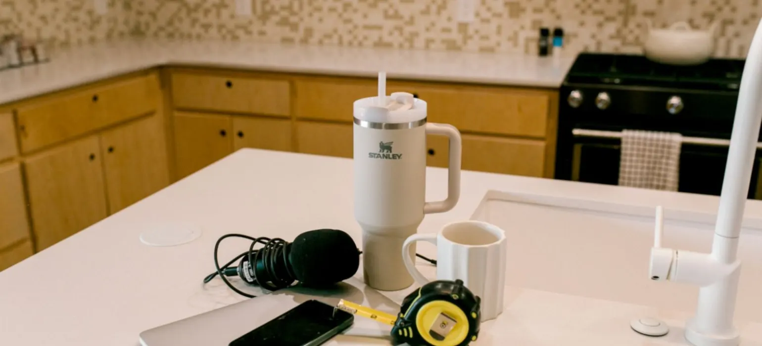 A laptop, phone, microphone, and mugs on a kitchen counter