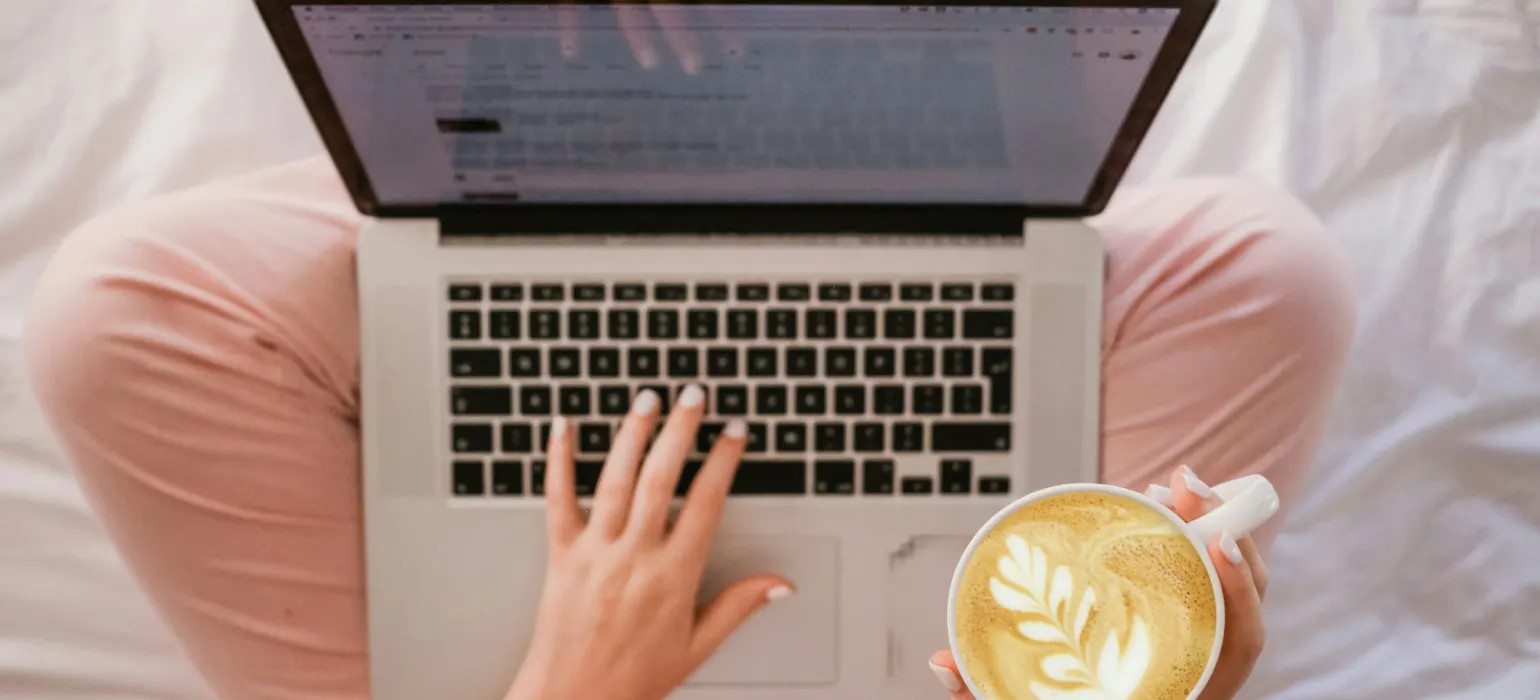 A person typing an email on a laptop with a coffee