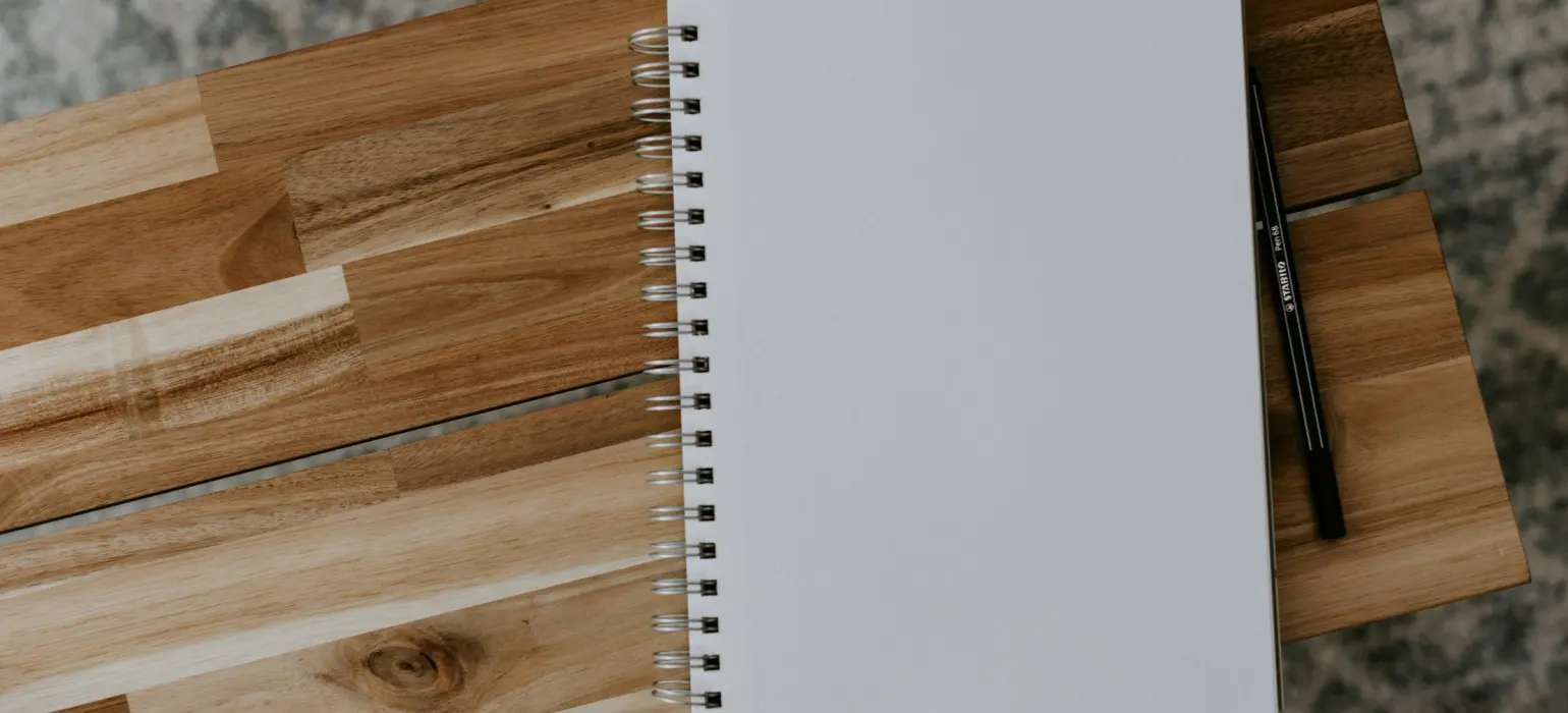A blank spiral notebook and pen on a wooden desk