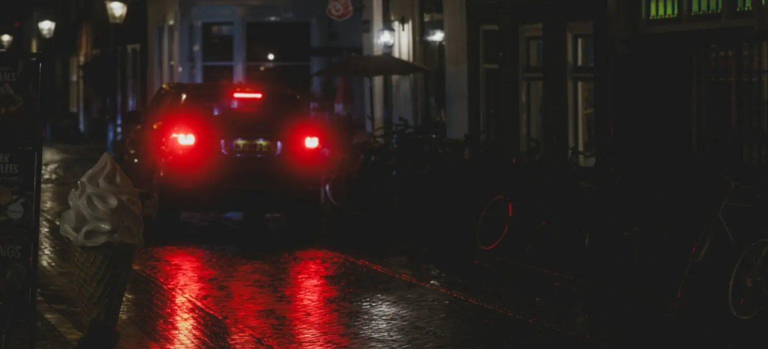 Car taillights reflect on wet city street at night