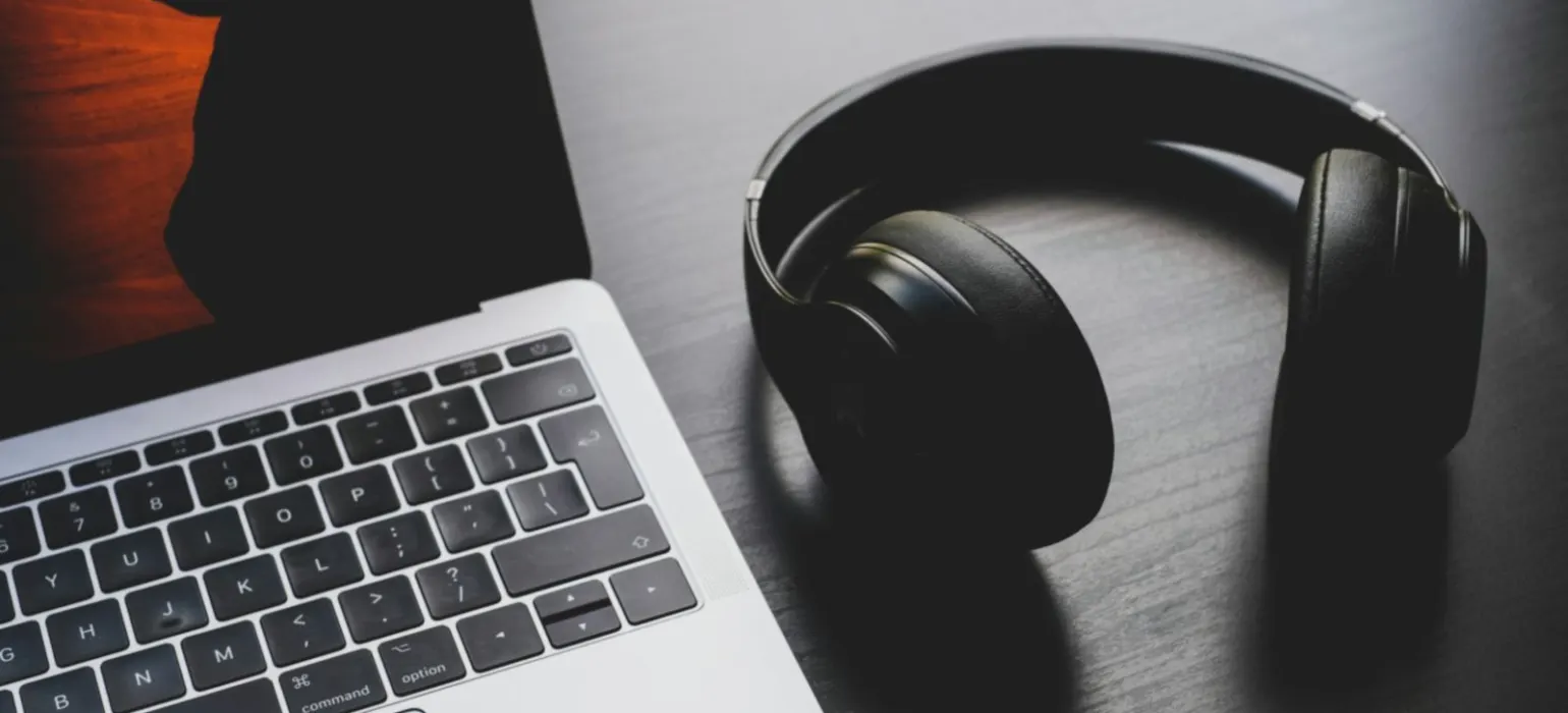 Black wireless headphones beside MacBook Pro