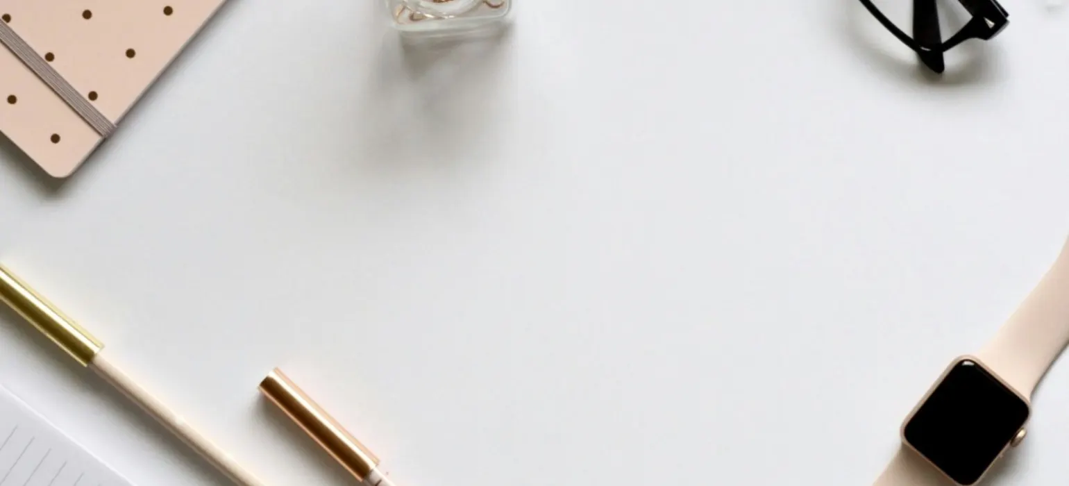 A tidy white desk with glasses, pens and a notebook